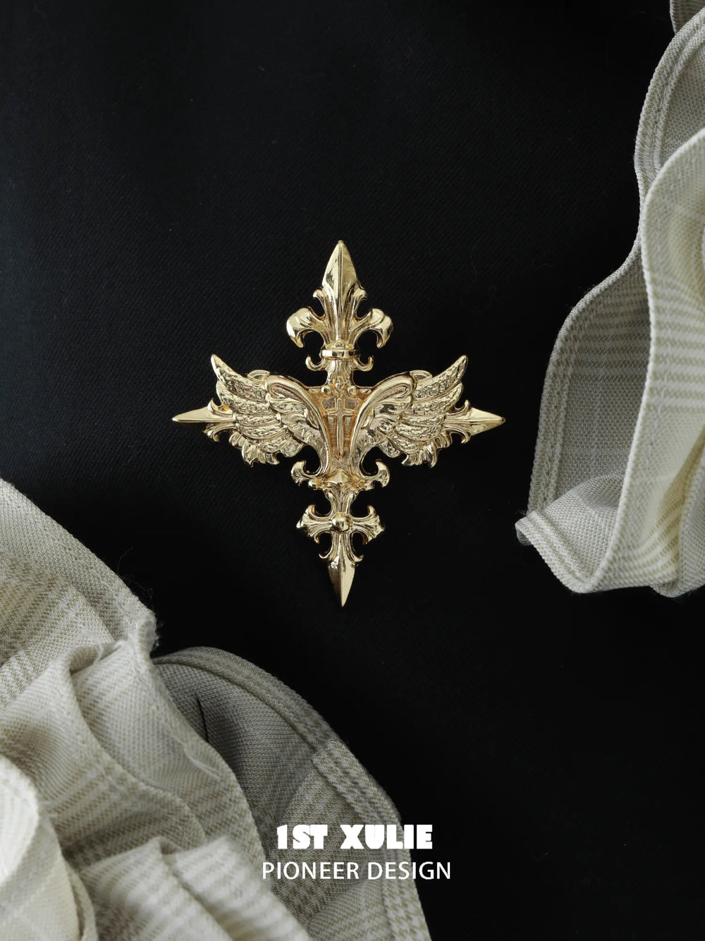 Gold-tone winged Fleur-de-Lis brooch on black fabric.