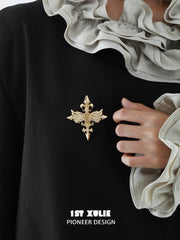 Gold-tone winged Fleur-de-Lis brooch worn with a light ruffled collar.