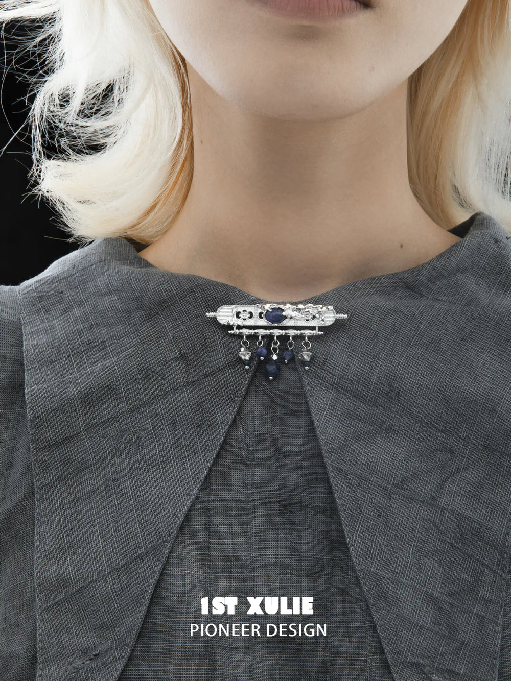 Blue stone brooch worn at the center of a grey shirt collar