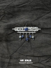 Blue bead tassel brooch laid on dark textured fabric