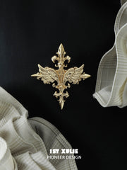 Gold-tone winged Fleur-de-Lis brooch on black fabric.
