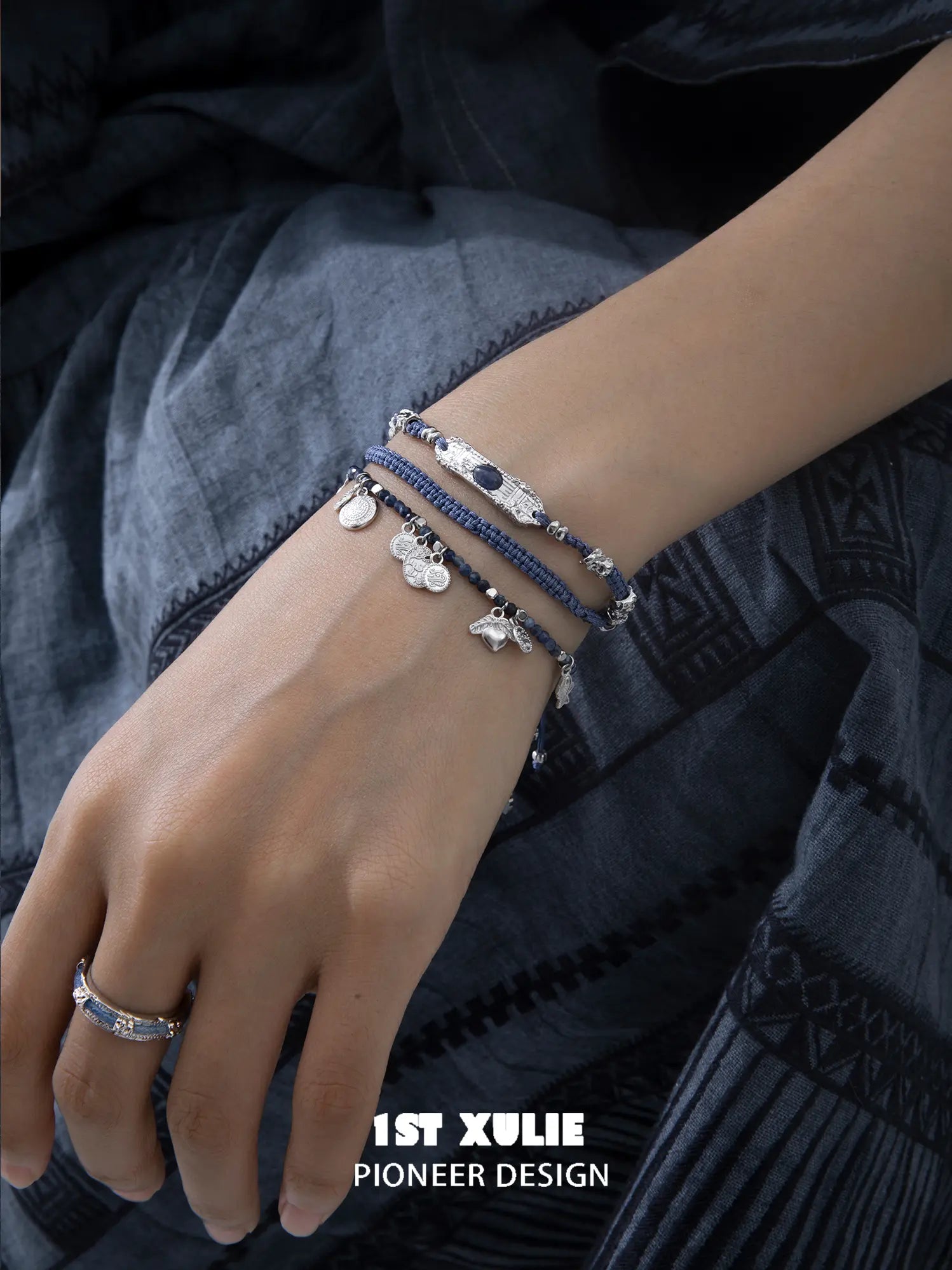 Blue beaded charm bracelet layered with blue cord bracelets and a bangle