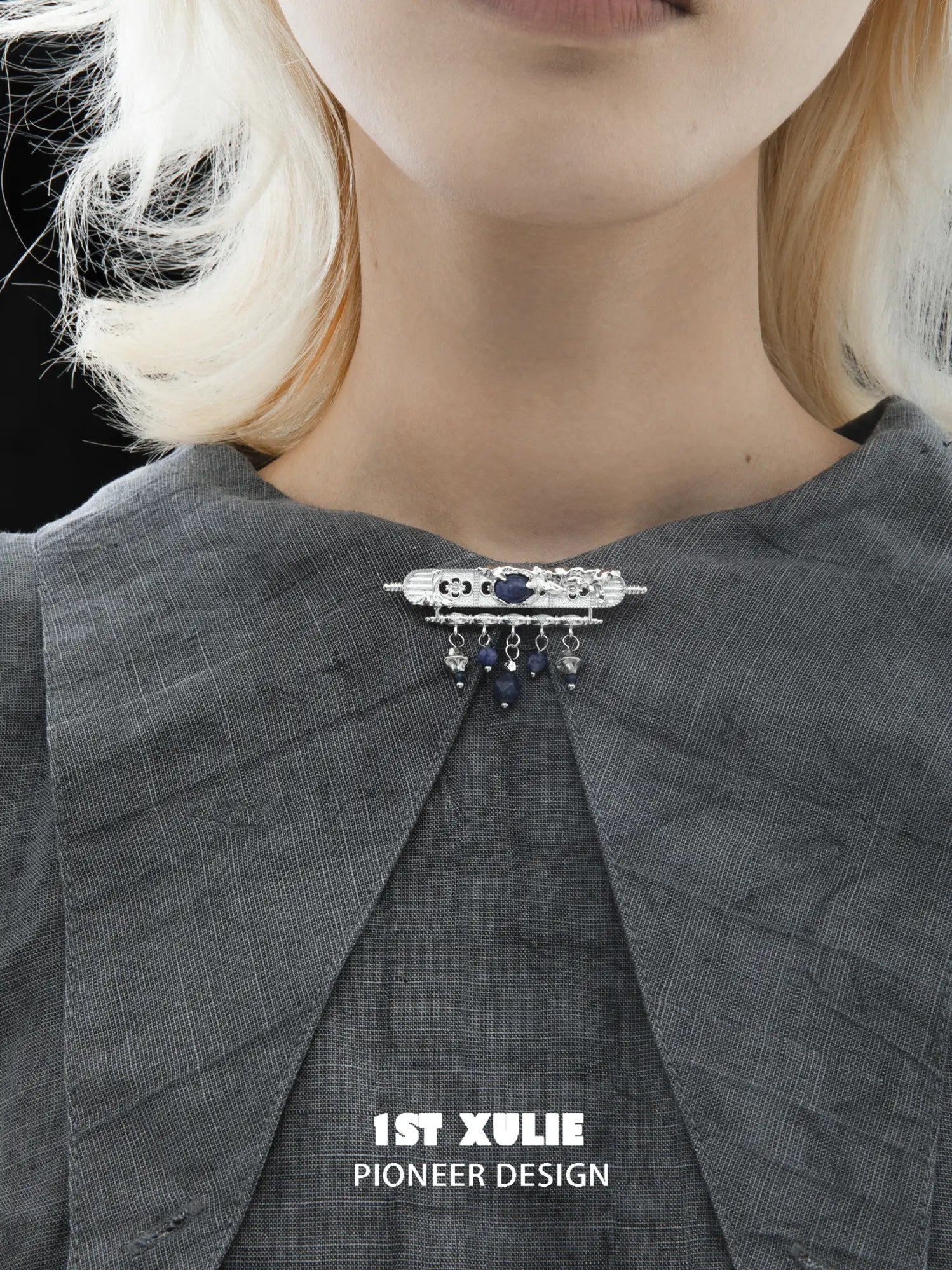 Blue stone brooch worn at the center of a grey shirt collar