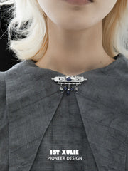 Blue stone brooch worn at the center of a grey shirt collar