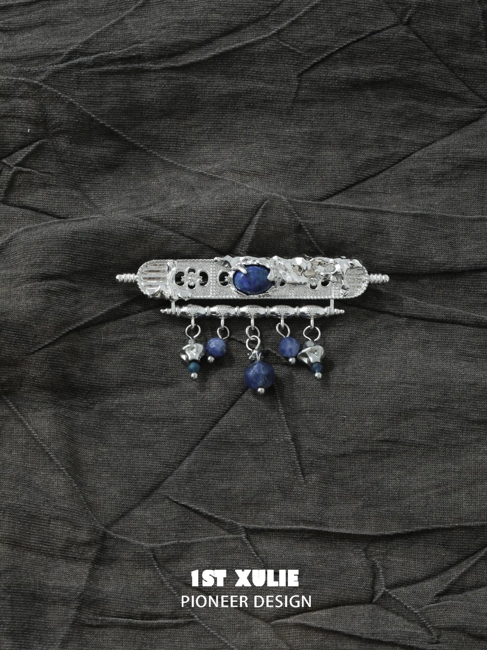 Blue bead tassel brooch laid on dark textured fabric