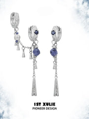 Asymmetrical hoop and tassel earring pair against a pale decorative background