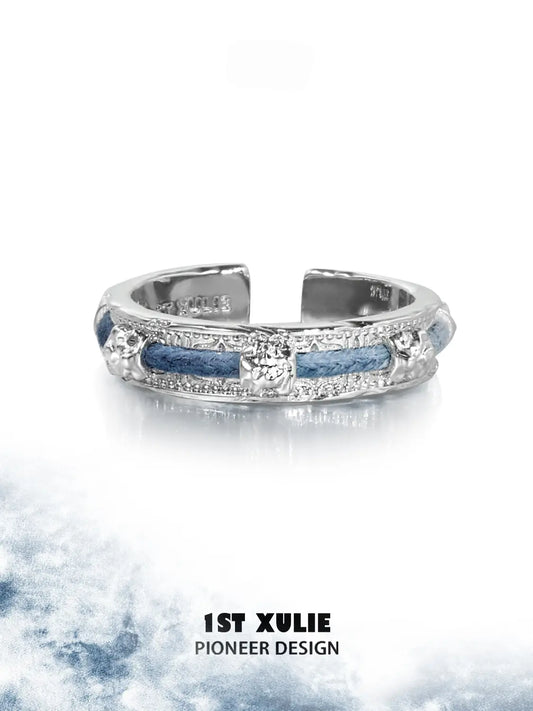 Narrow blue woven ring displayed against a light cloud-pattern background