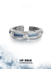 Narrow blue woven ring displayed against a light cloud-pattern background