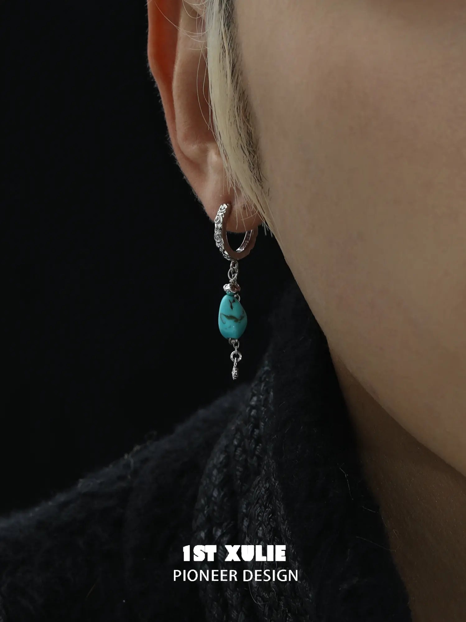 Close-up of a turquoise drop earring worn beside a dark collar
