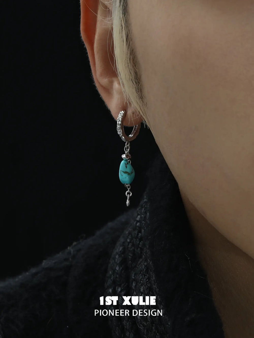 Close-up of a turquoise drop earring worn beside a dark collar