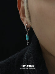 Close-up of a turquoise drop earring worn beside a dark collar
