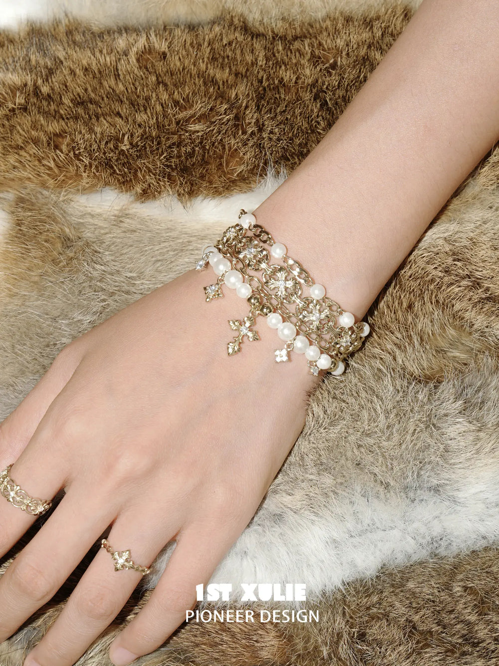Layered pearl-bead and fleur-de-lis bracelet worn with coordinating jewelry