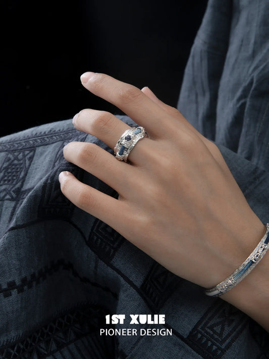 Wide woven ring worn on the hand beside a narrow coordinating ring